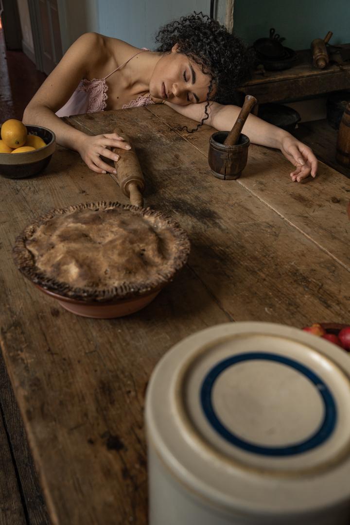 a woman laying on a table touching a rolling pin with other cooking tools around her